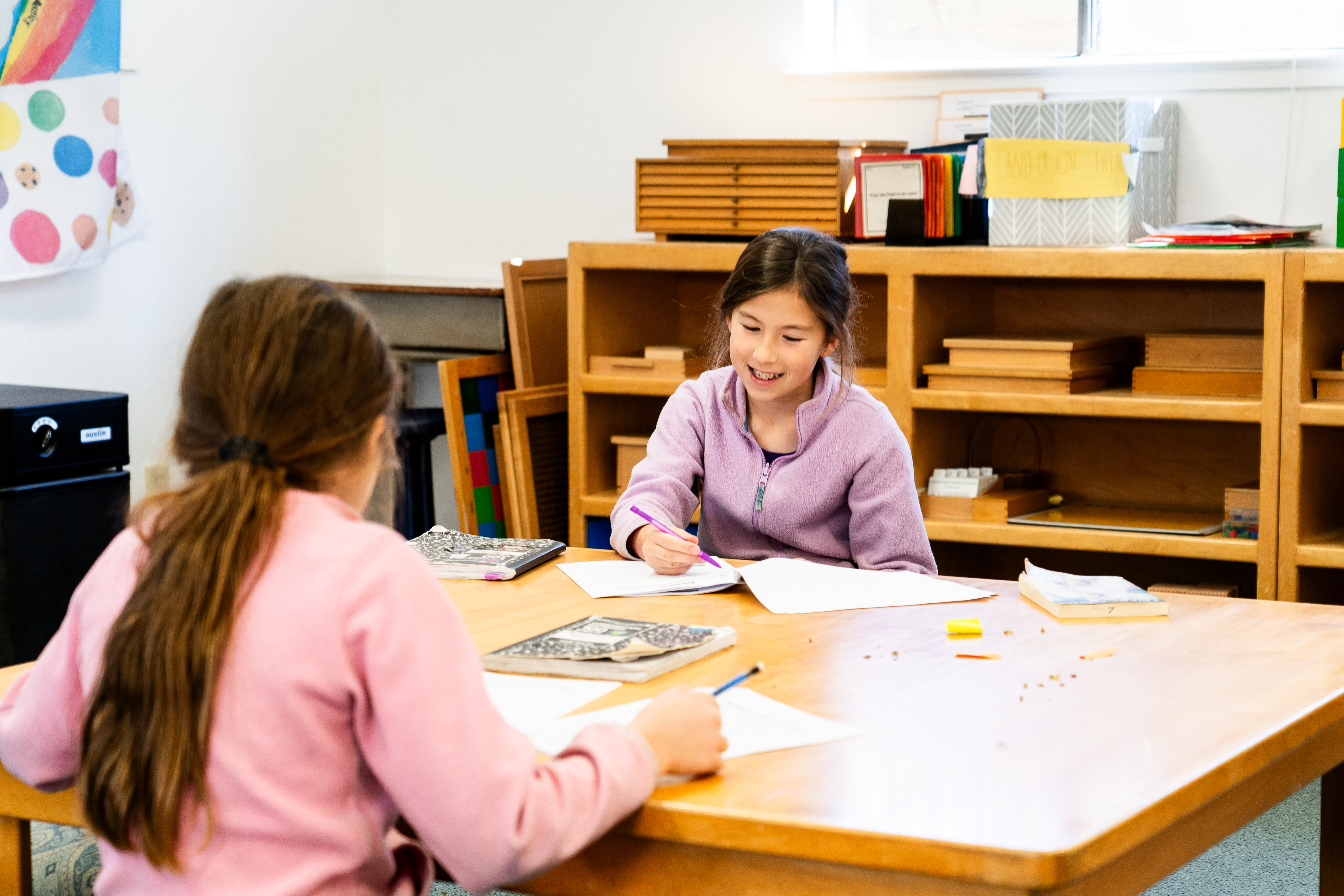 Montessori children are sitting at a table in a classroom.