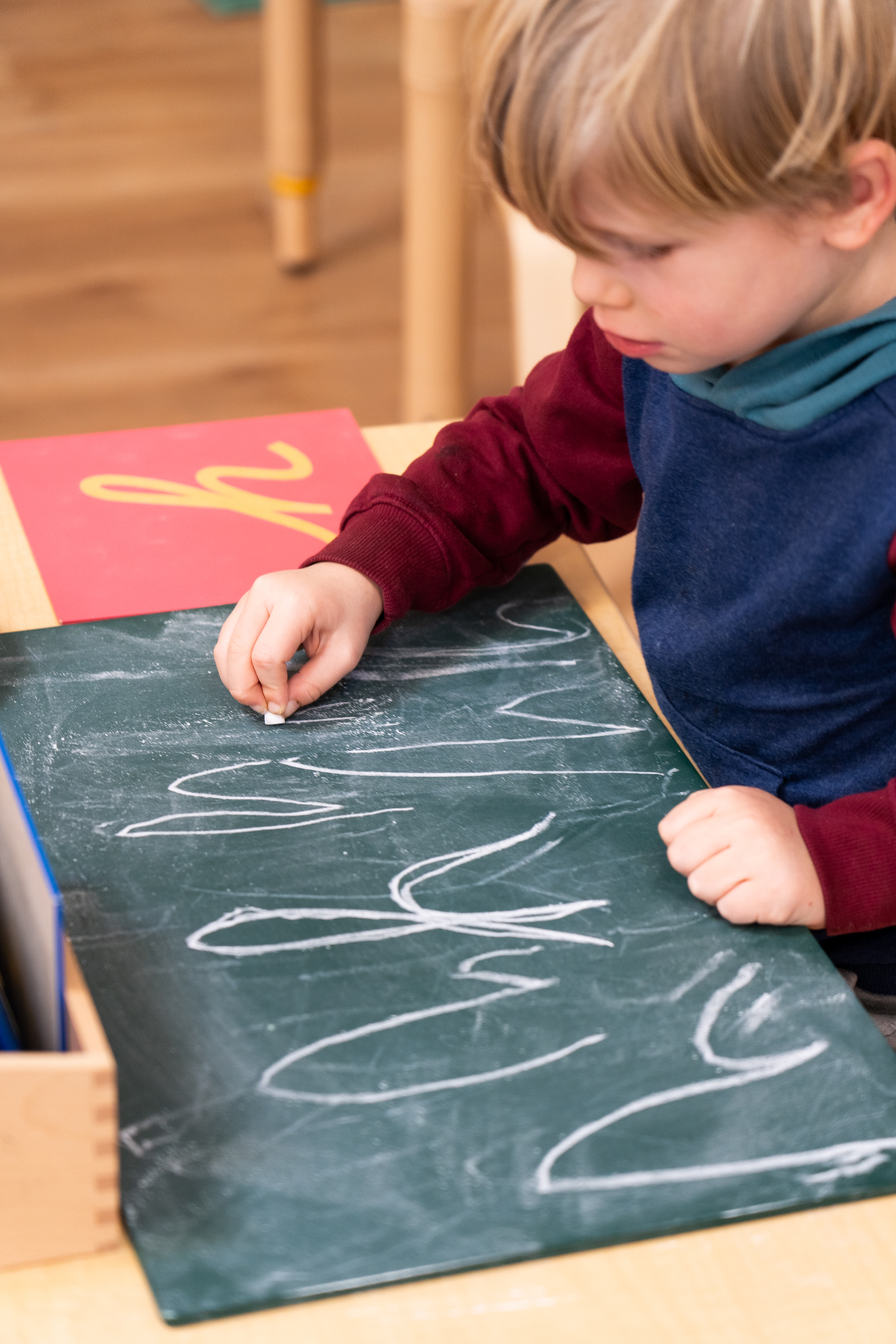 A Montessori child  is writing on a blackboard with chalk.
