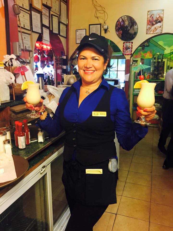 A woman in a blue shirt and black vest is holding two drinks