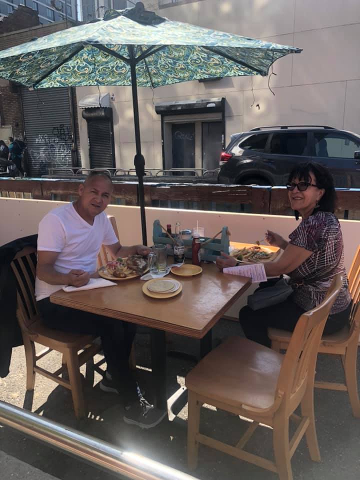 A man and a woman are sitting at a table under an umbrella eating food.