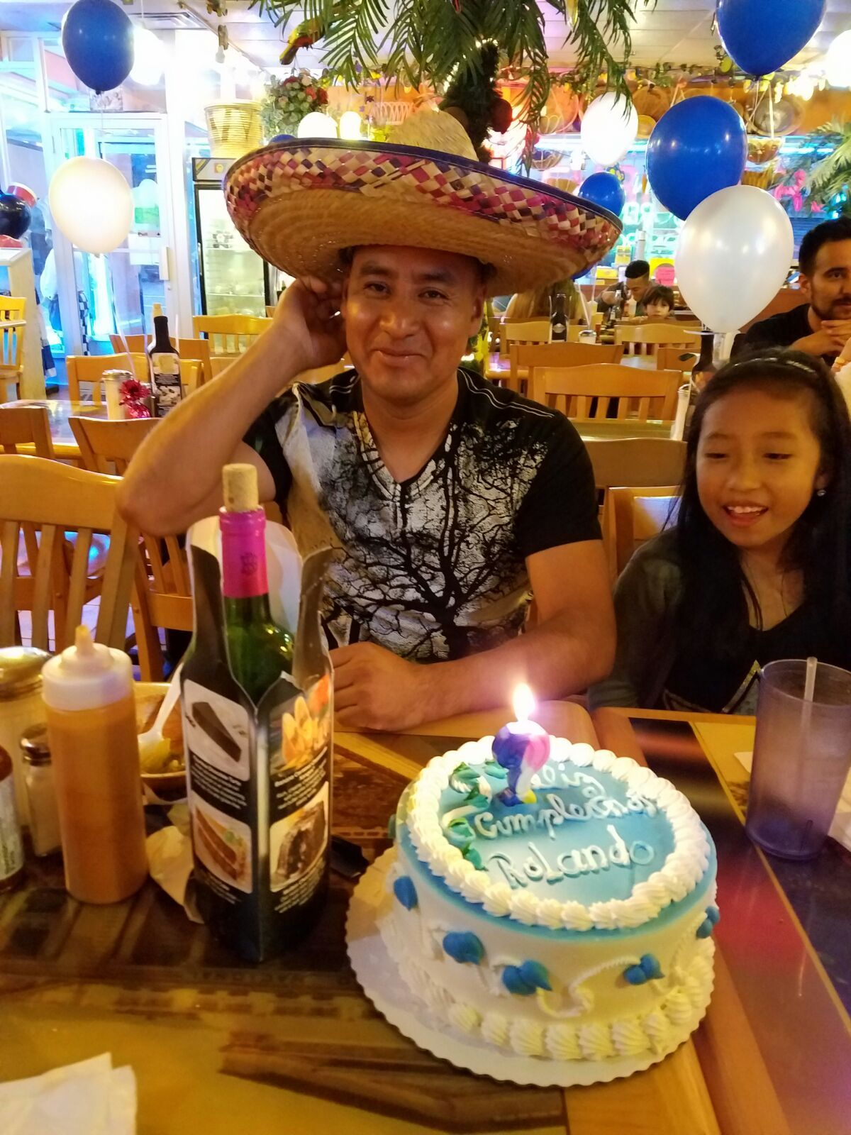 A man wearing a sombrero is sitting at a table with a birthday cake