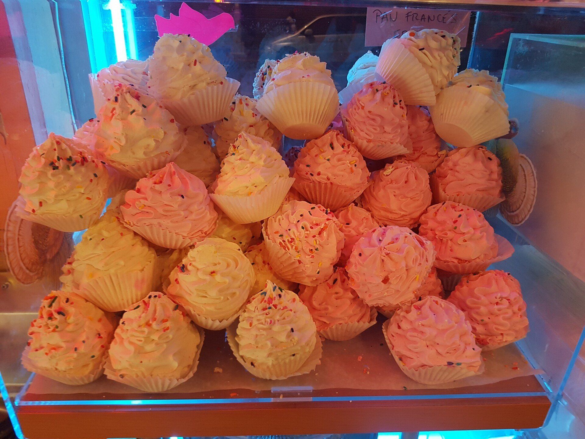 A display case filled with cupcakes with pink frosting and sprinkles.
