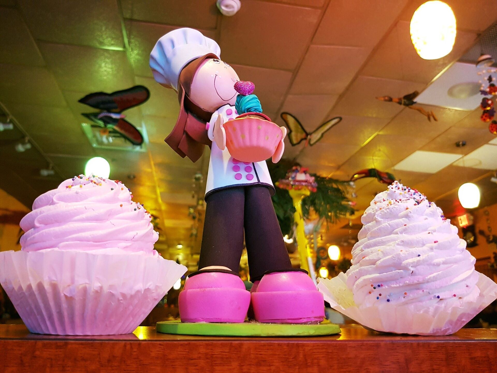 A figurine of a chef holding a cupcake is surrounded by giant cupcakes