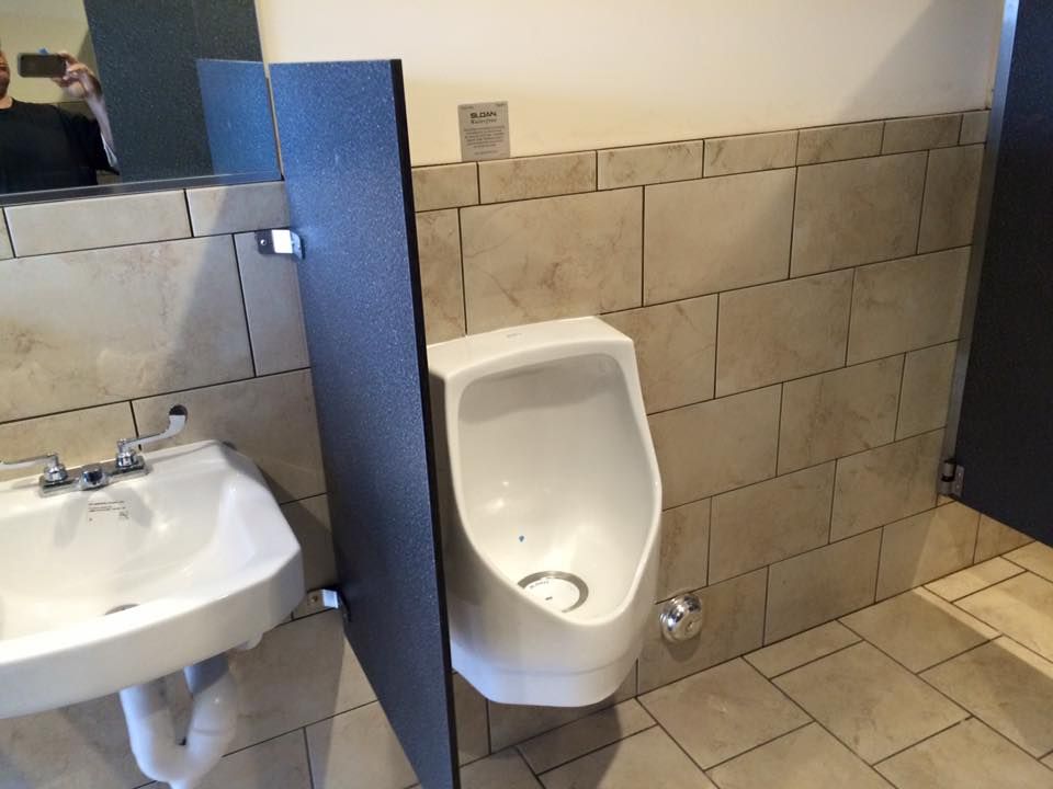 A bathroom with a urinal , sink and mirror
