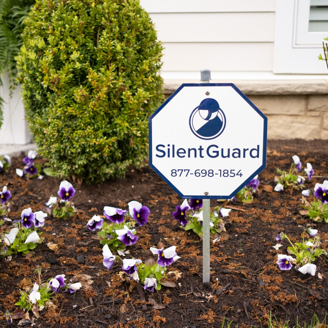 A sign that says silent guard in a garden