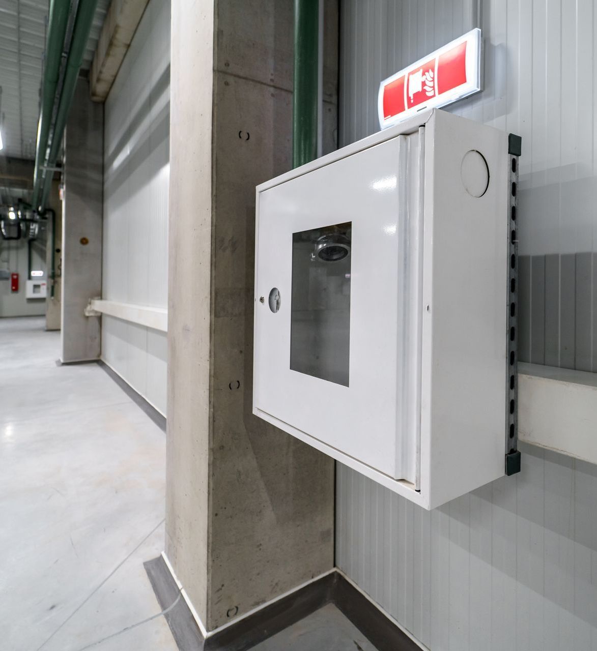 A white fire hydrant box is hanging on a wall in a building.