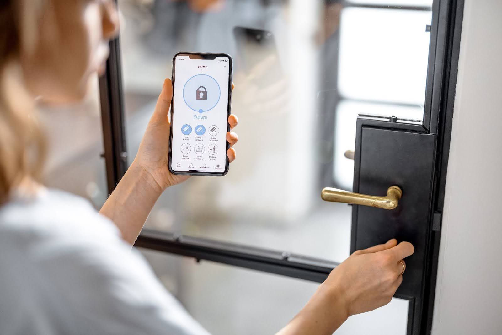A person uses a smartphone app to unlock a smart door lock on a glass door.