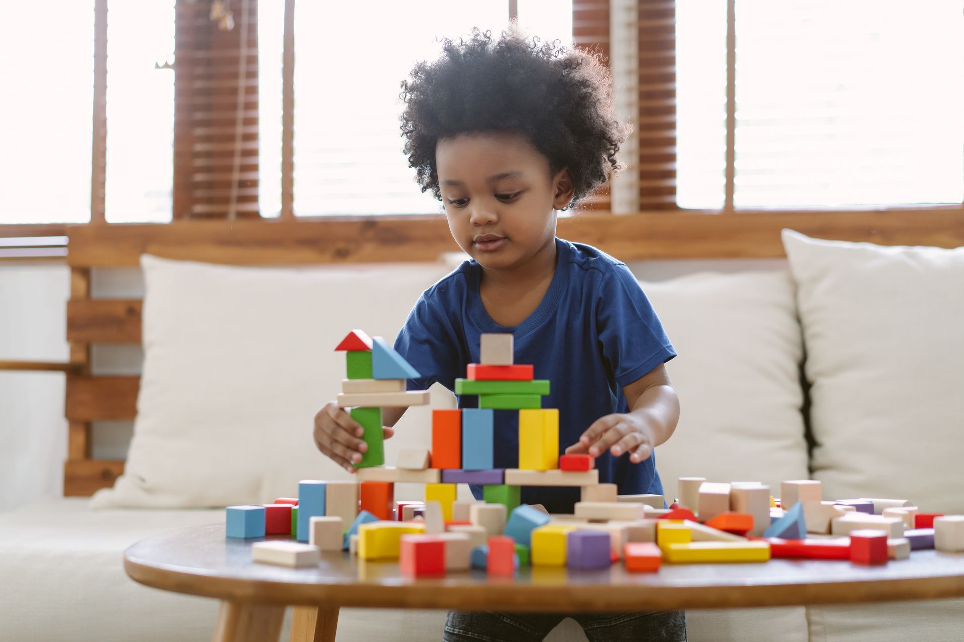 A young boy is playing with colorful blocks on a table in a family room.