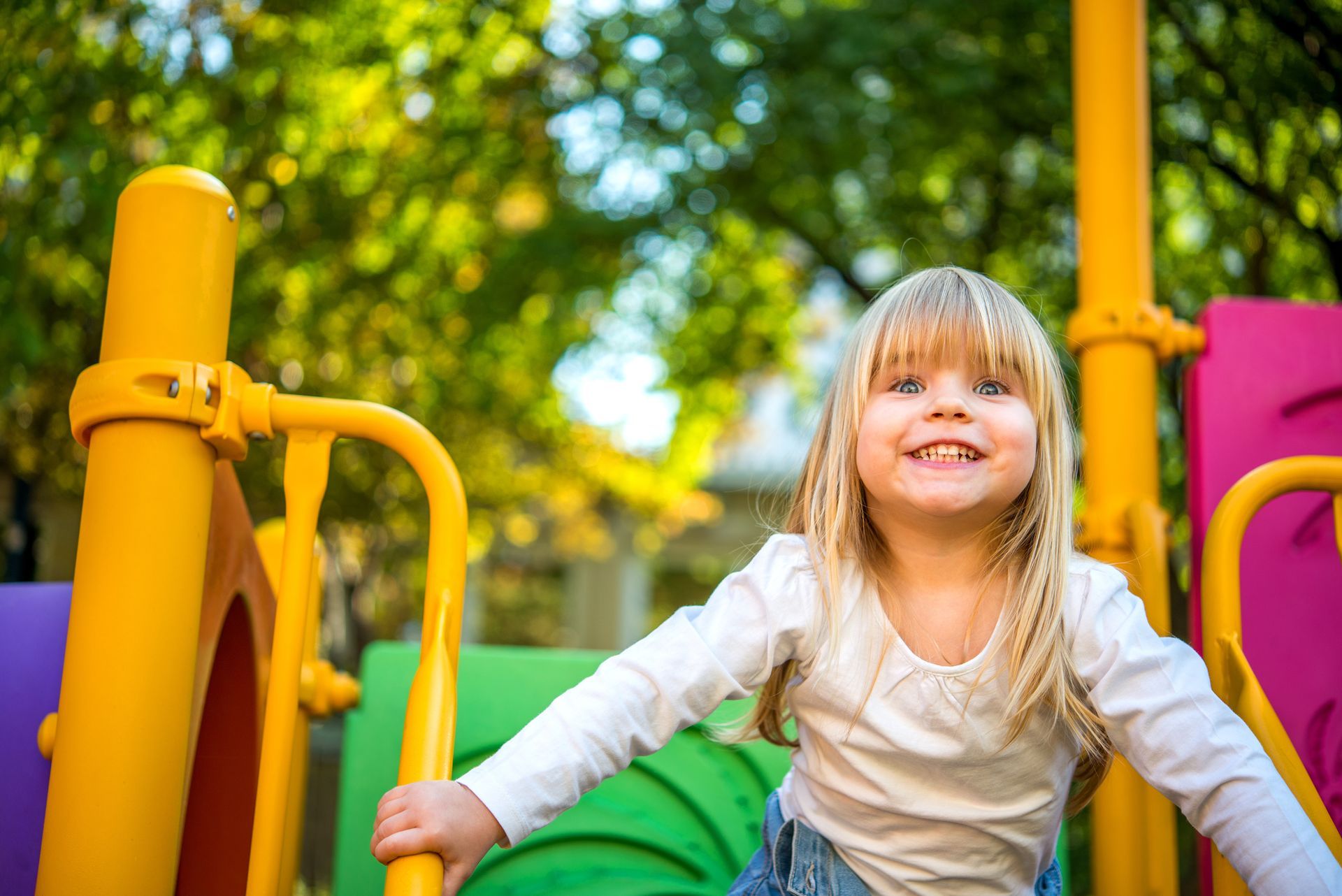 Young girl is on a colorful playground in the park. She is smiling.