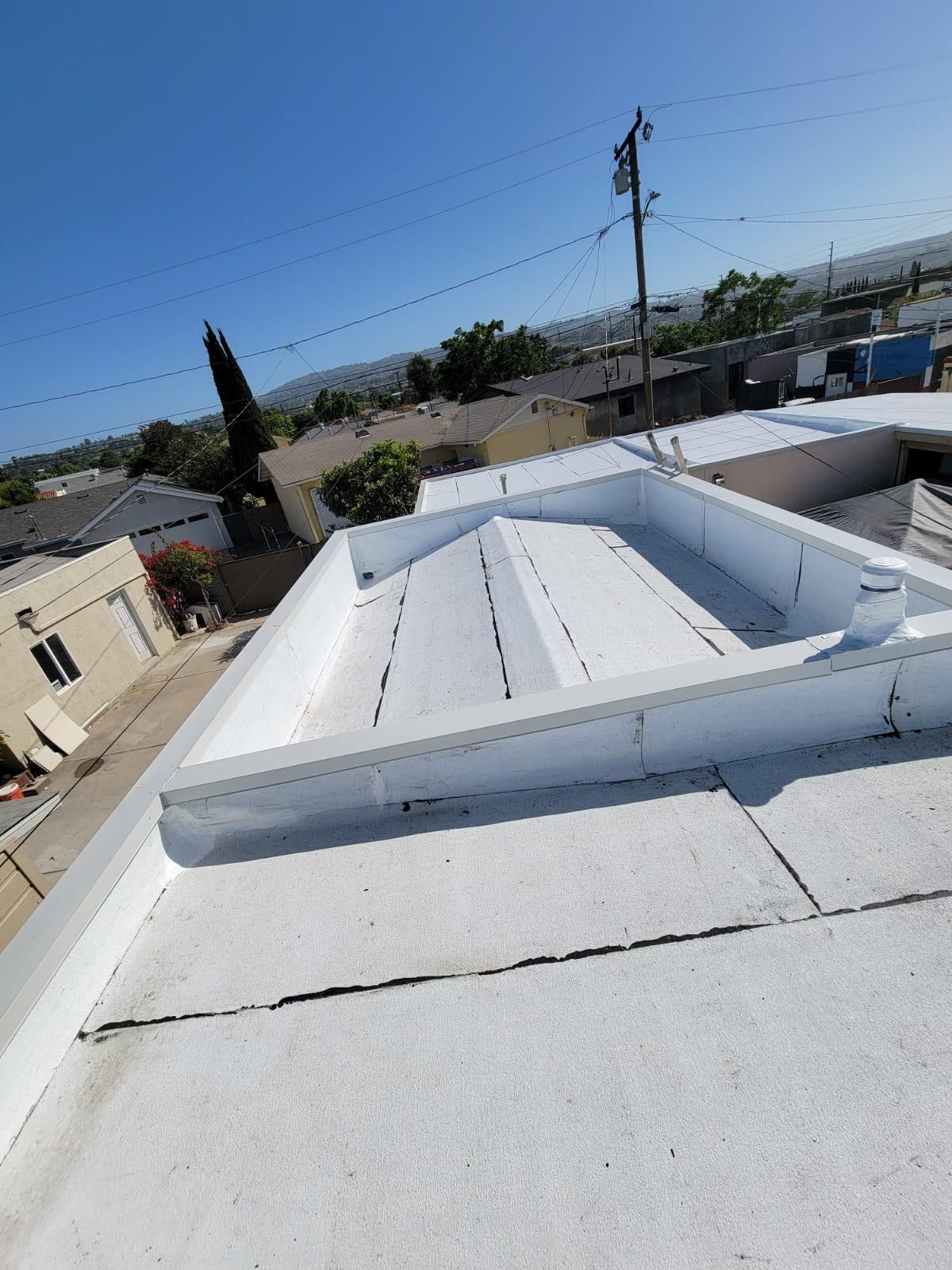 White metal rooftop with a skylight, viewed over a neighborhood under a clear blue sky.