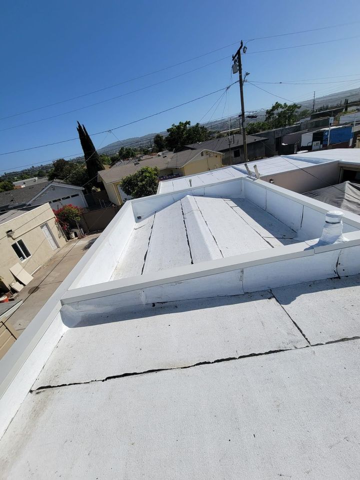 White metal rooftop with a skylight, viewed over a neighborhood under a clear blue sky.