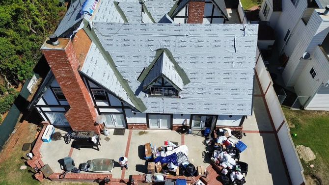 Worker installing shingles on a steep roof with a nail gun on a sunny day