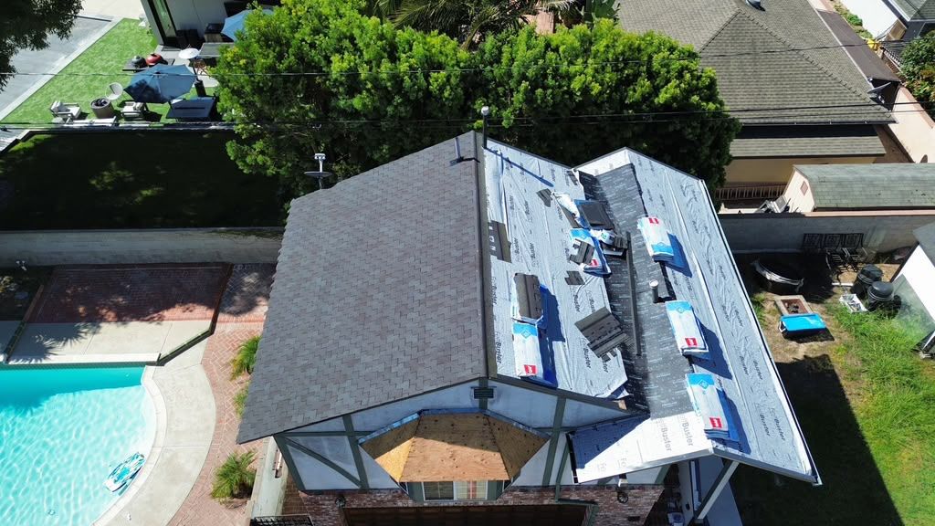 Aerial view of a house with a dark roof beside a backyard pool and patio umbrellas