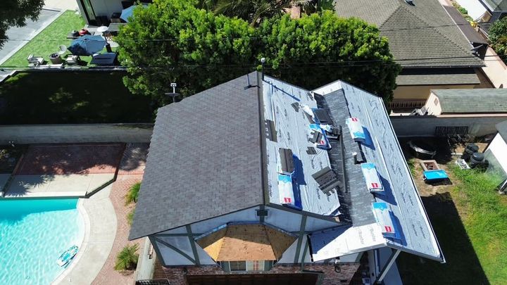 Aerial view of a house with a dark roof beside a backyard pool and patio umbrellas