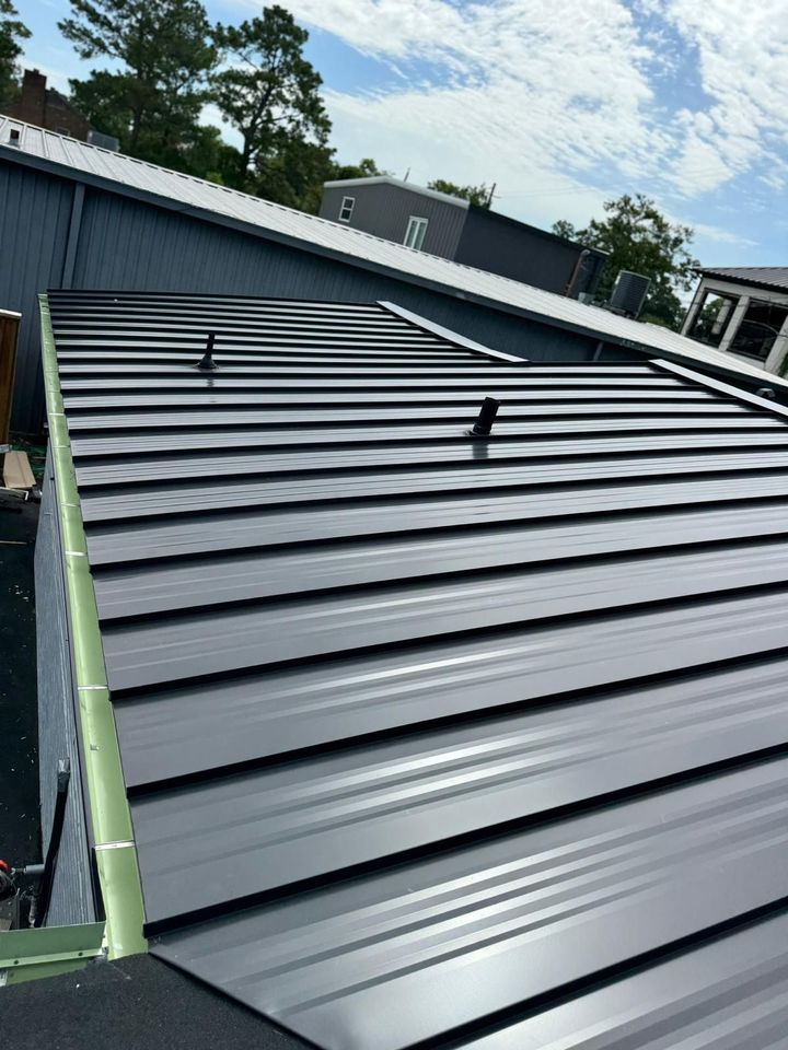 Black metal roof on a sloped building under construction, with trees and sky in the background