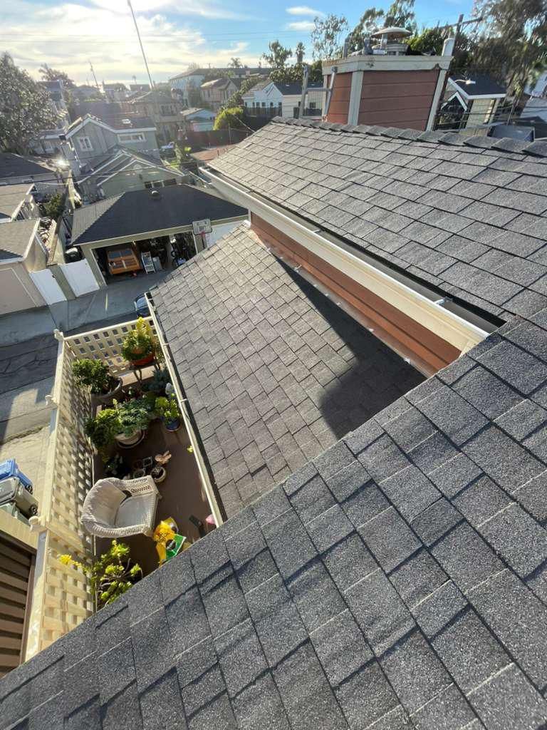 Rooftop view of gray shingled roofs, chimneys, and a small garden patio in a sunny neighborhood