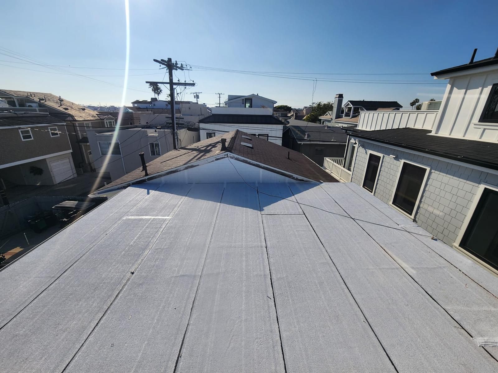 Rooftop view of a flat gray roof with neighboring houses and power lines under a clear blue sky
