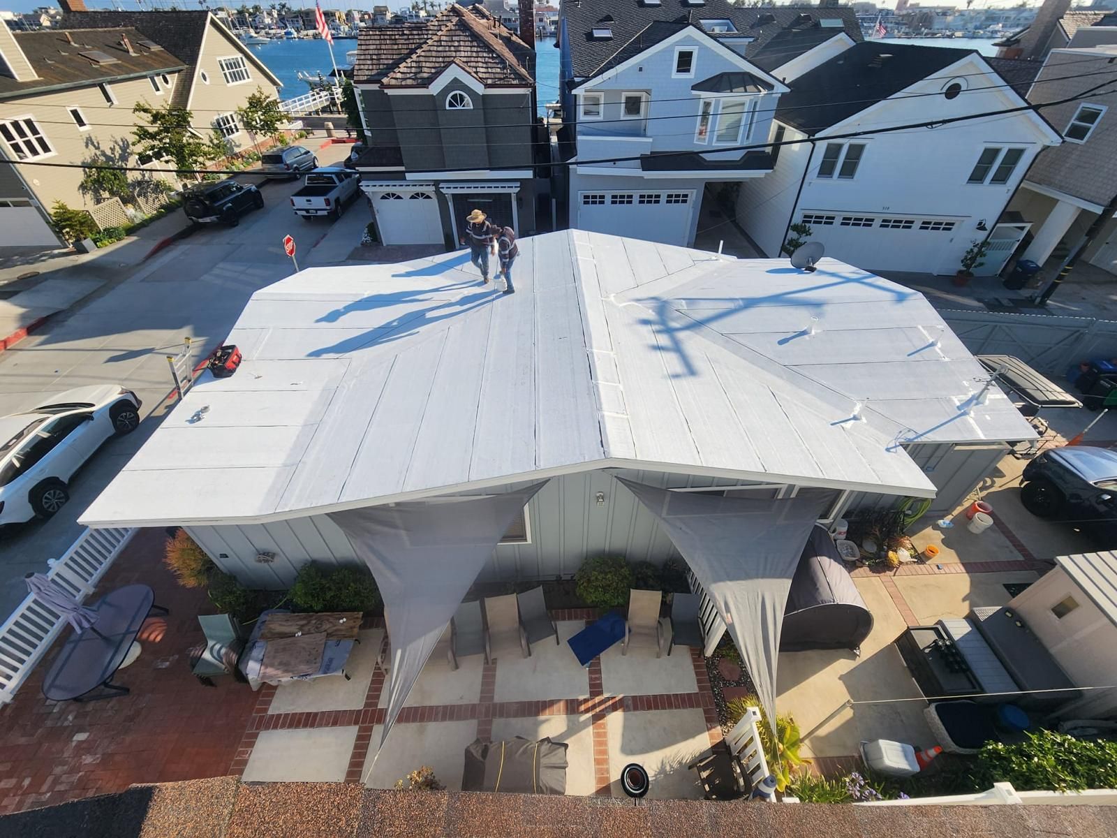 Aerial view of a white-roofed house under construction with workers on the roof in a residential neighborhood