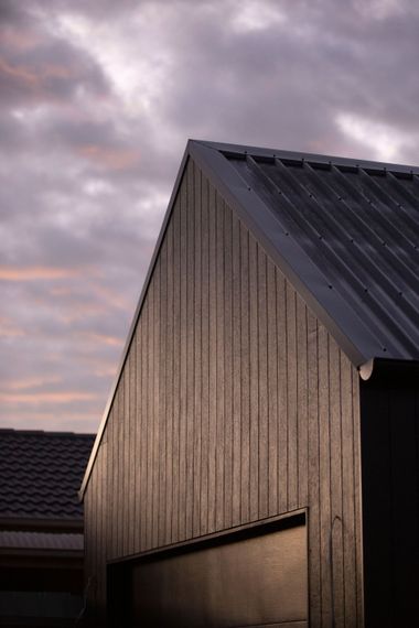 Modern wooden house gable with dark metal roof under a cloudy sunset sky