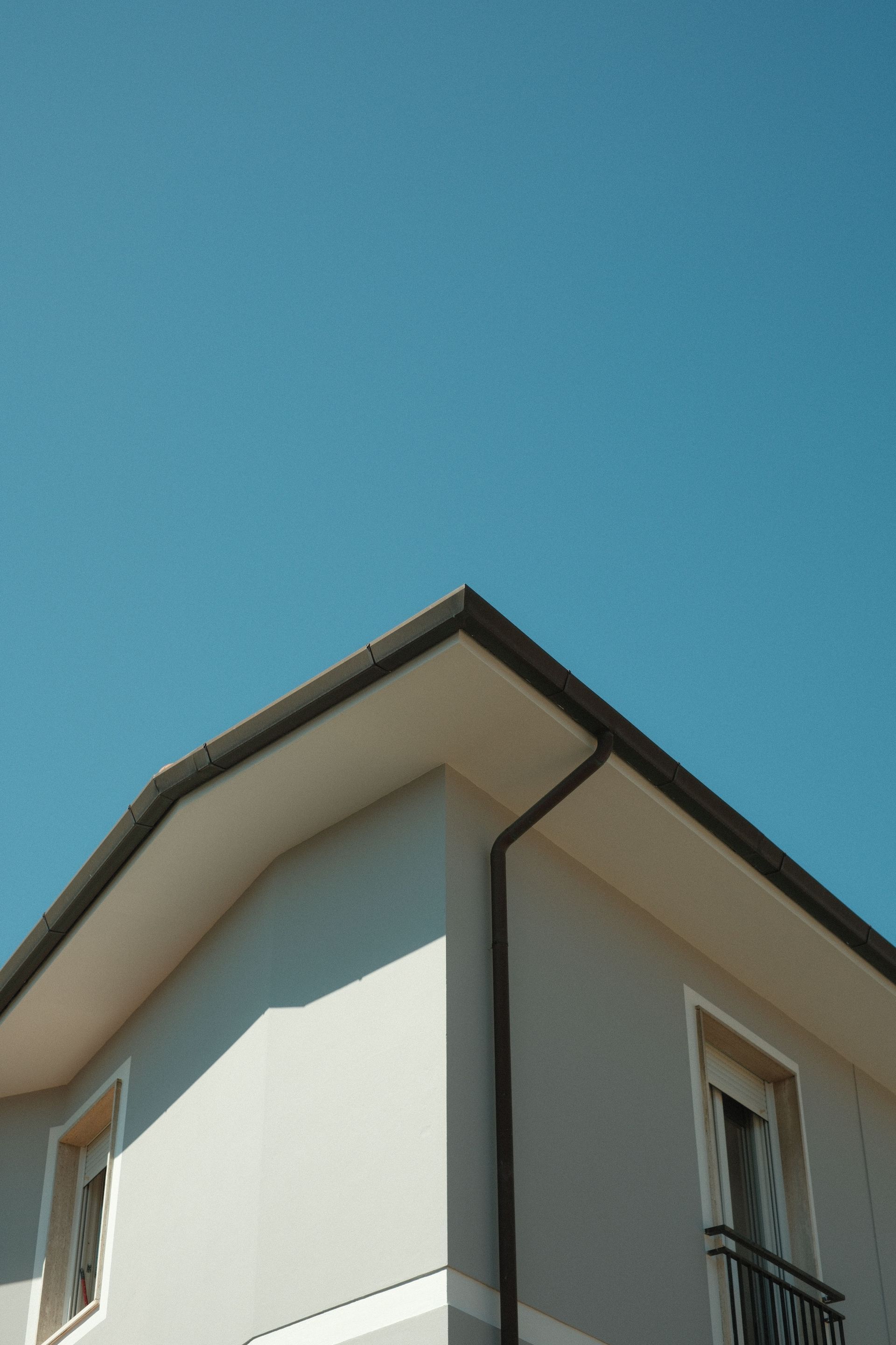 Corner of a modern white house with a dark roof against a clear blue sky