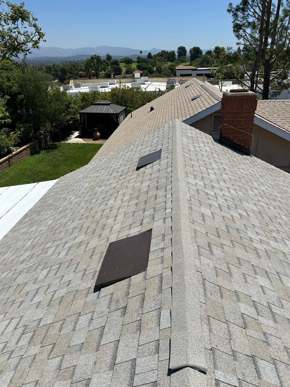 Rooftop view of a flat gray roof with neighboring houses and power lines under a clear blue sky