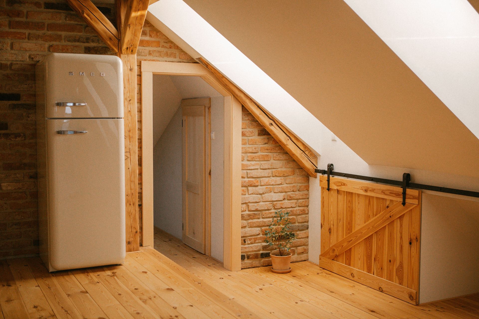Attic room with slanted ceiling, wooden floor, refrigerator, doorway, and wooden railing
