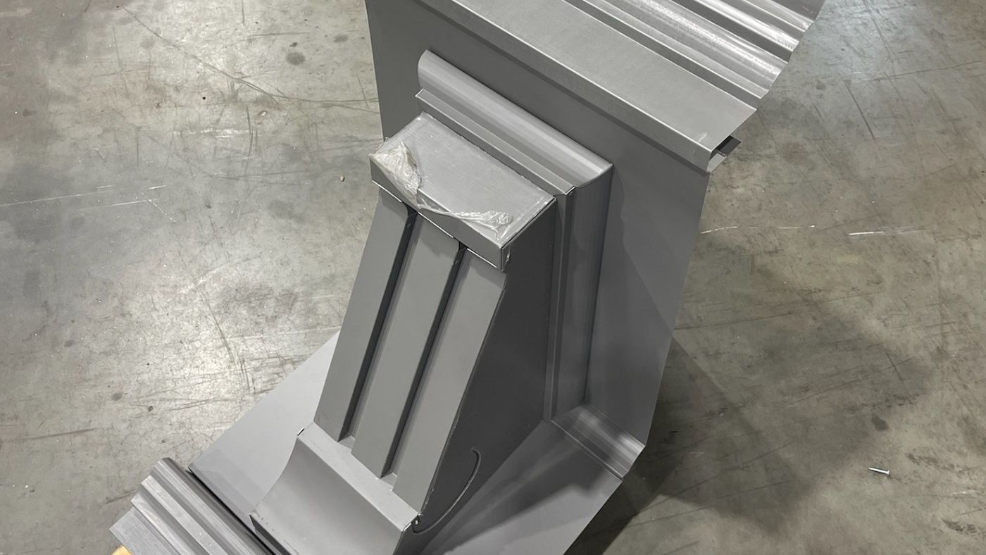 Close view of a gray formed assembly with curved transitions, stepped edges, and several changes in direction.