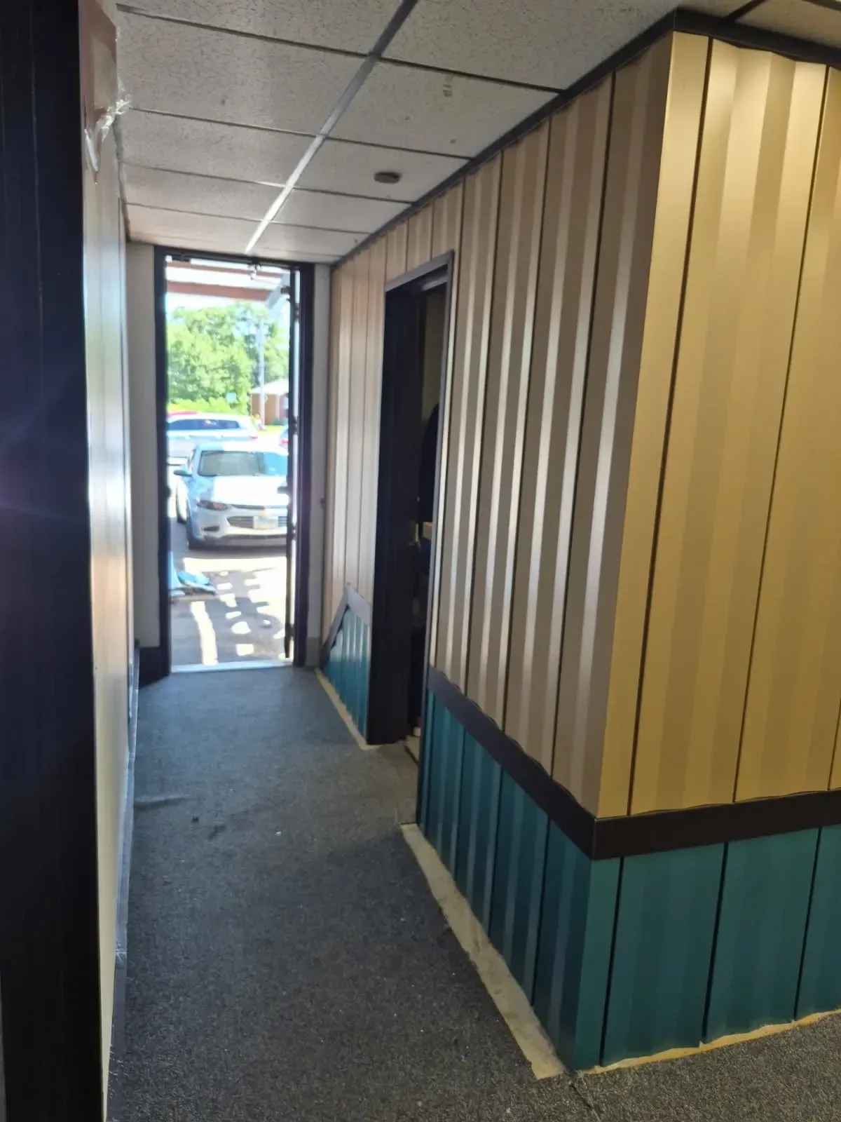 Interior corridor with lighter upper panels, blue lower panels, and dark trim continuing around a corner.