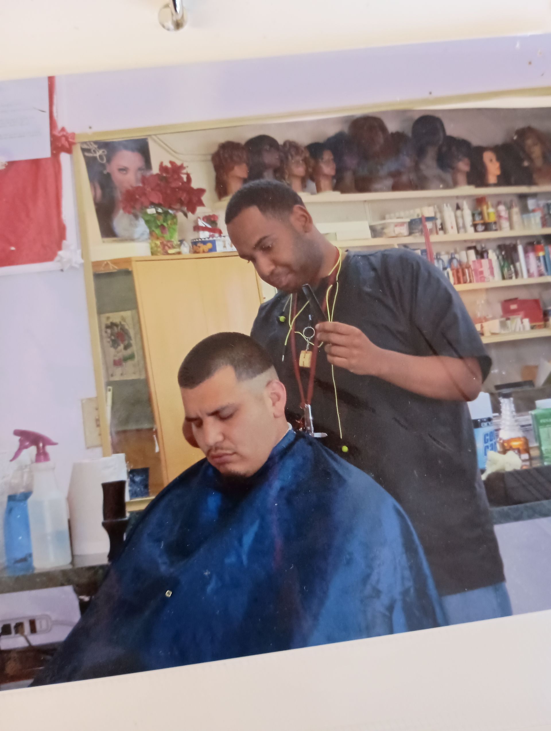 A man is getting his hair cut by a man in a blue cape