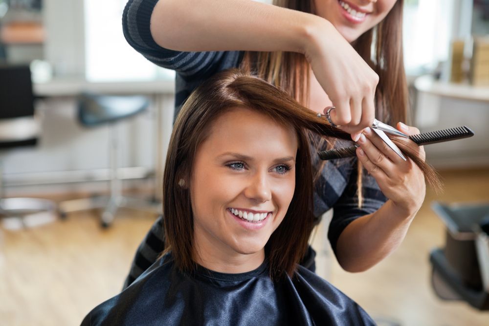 A woman is getting taught how to cut hair by a hairdresser in a salon.