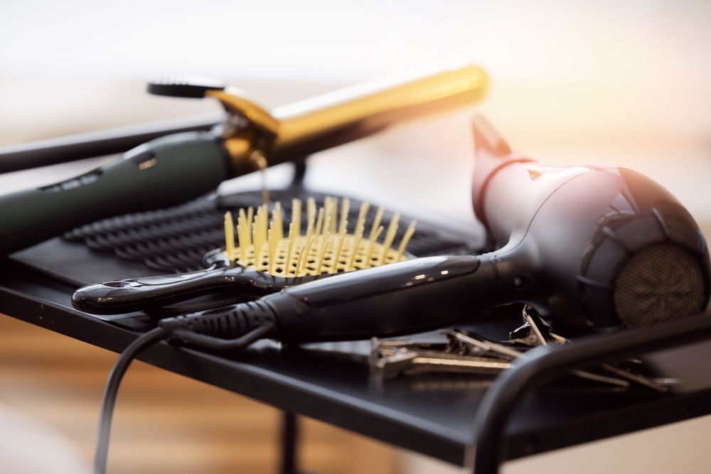 A hair dryer , comb , curling iron and scissors are on a table.