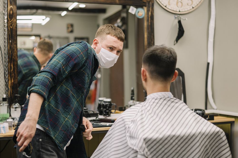 A man is getting his hair cut by a barber wearing a mask.