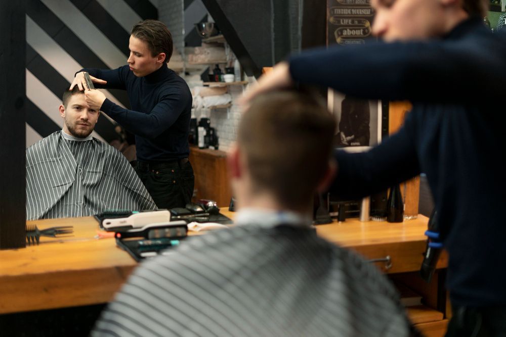 A man is getting his hair cut by a barber in a barber shop. 