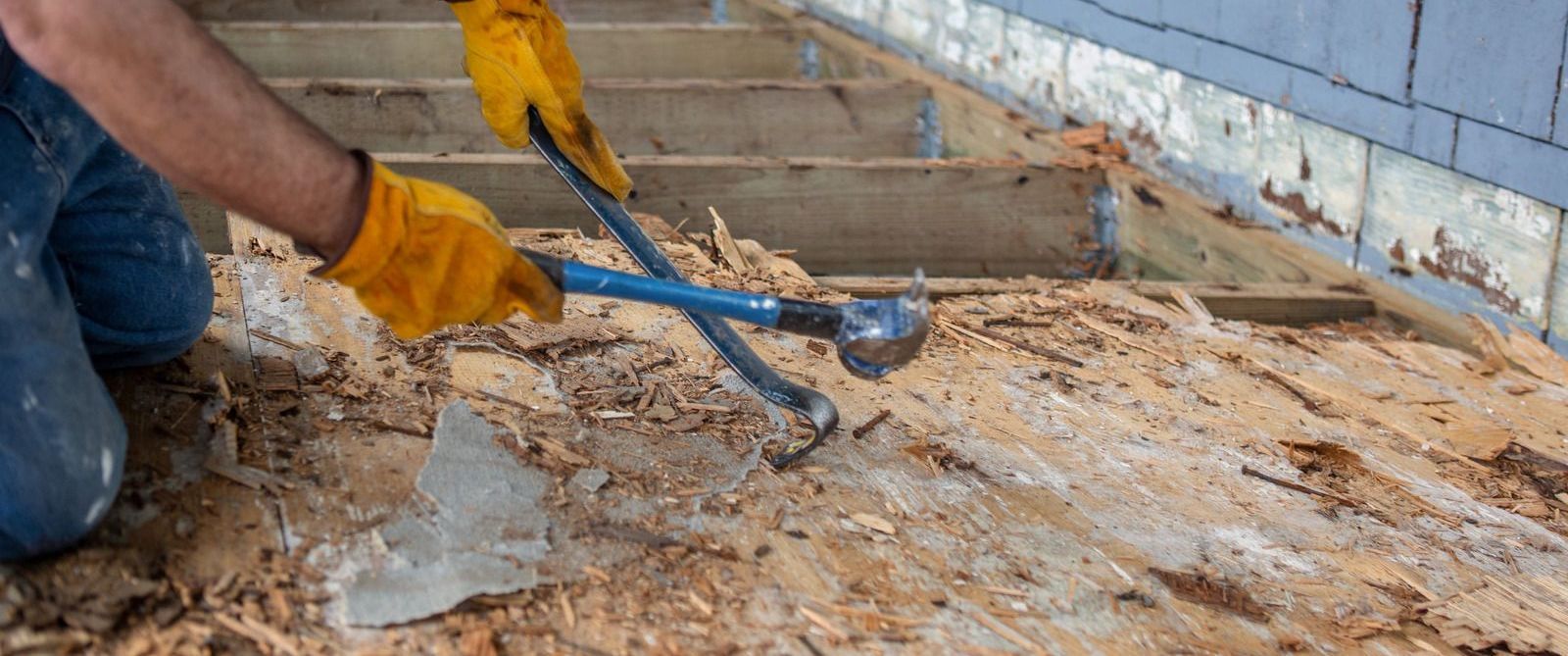 Person wearing yellow gloves uses a tool to remove wood from a surface.
