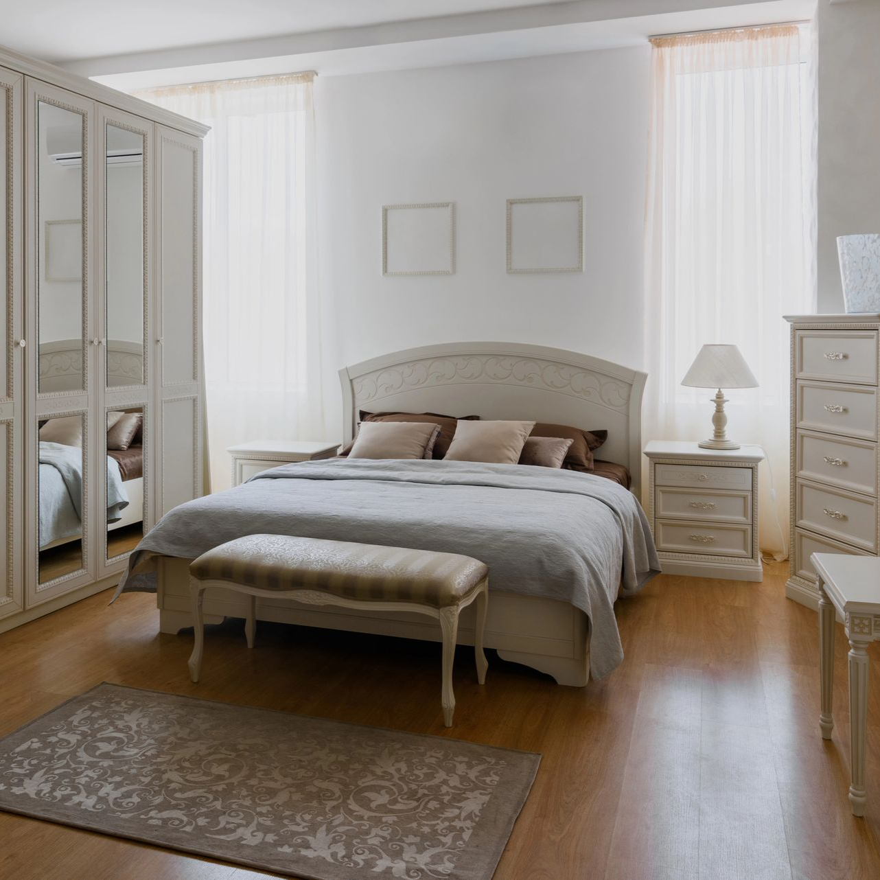 Camera da letto con mobili bianchi, letto, panca, tappeto e finestre.
