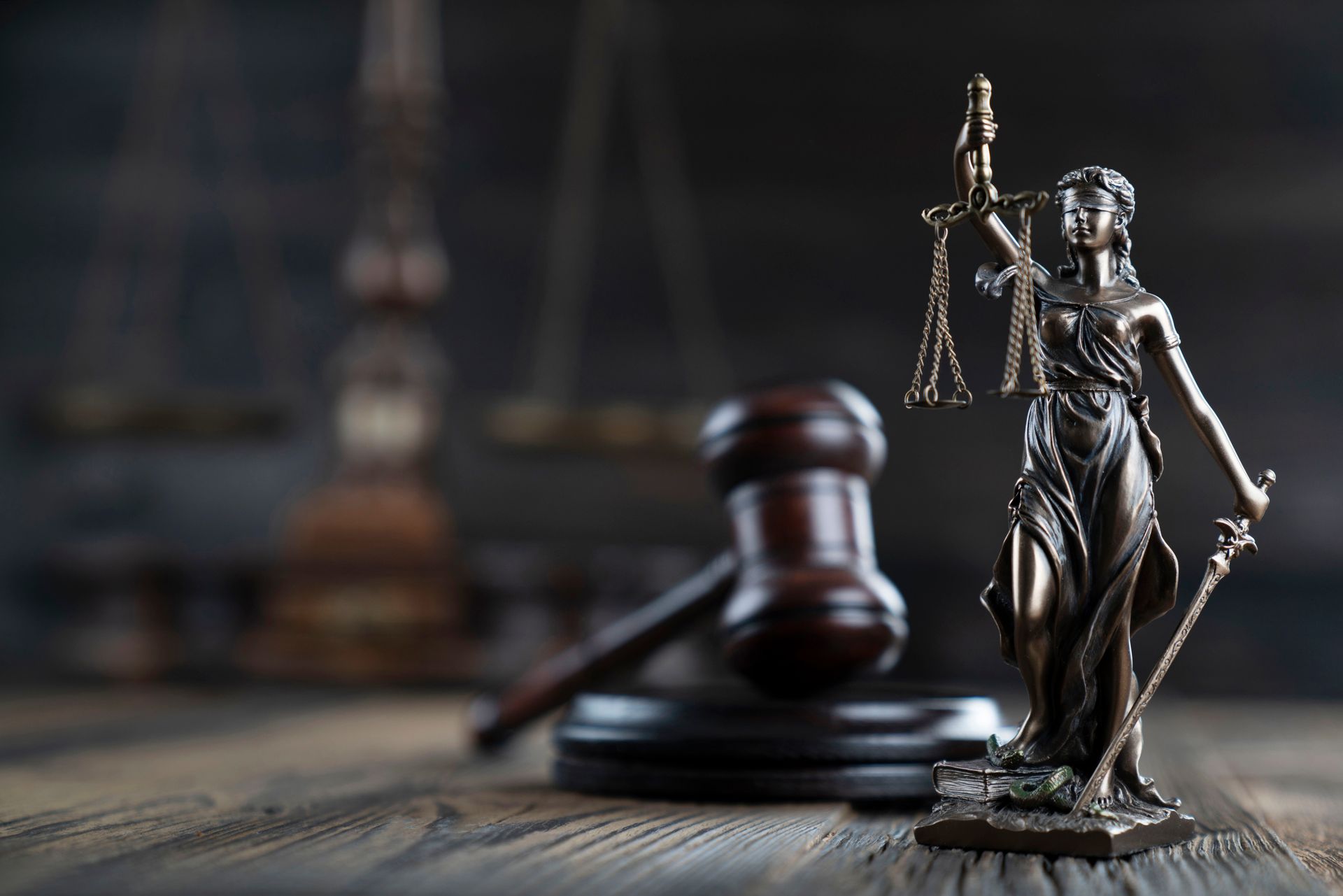A statue of justice is sitting on a wooden table next to a wooden gavel.