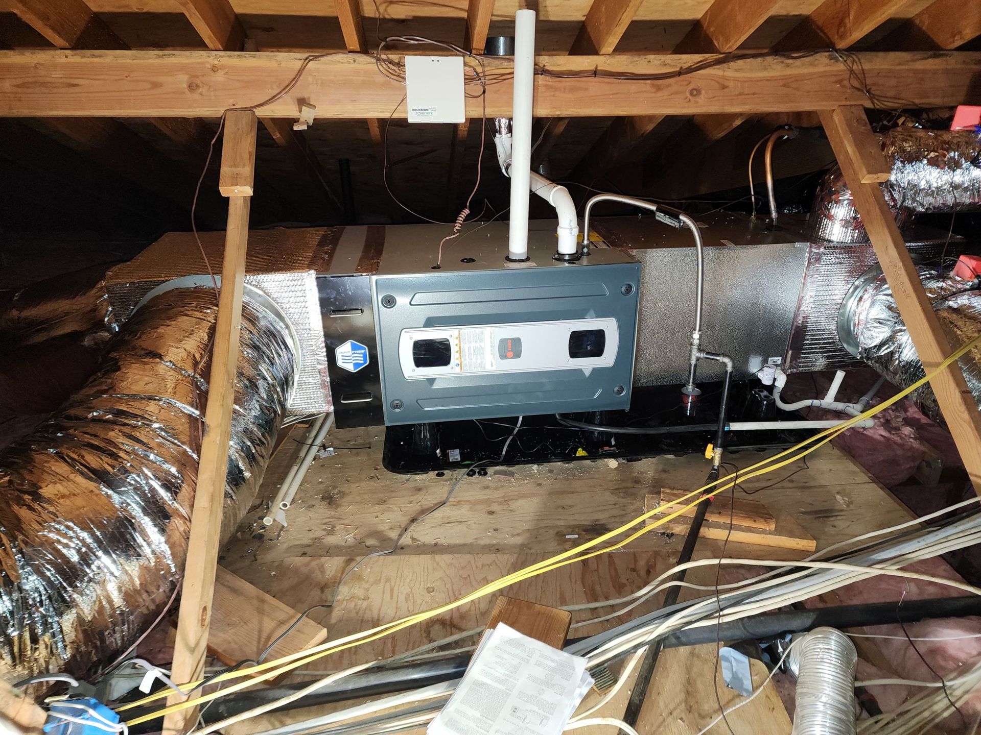 HVAC unit in an attic, with ductwork and exposed framing.