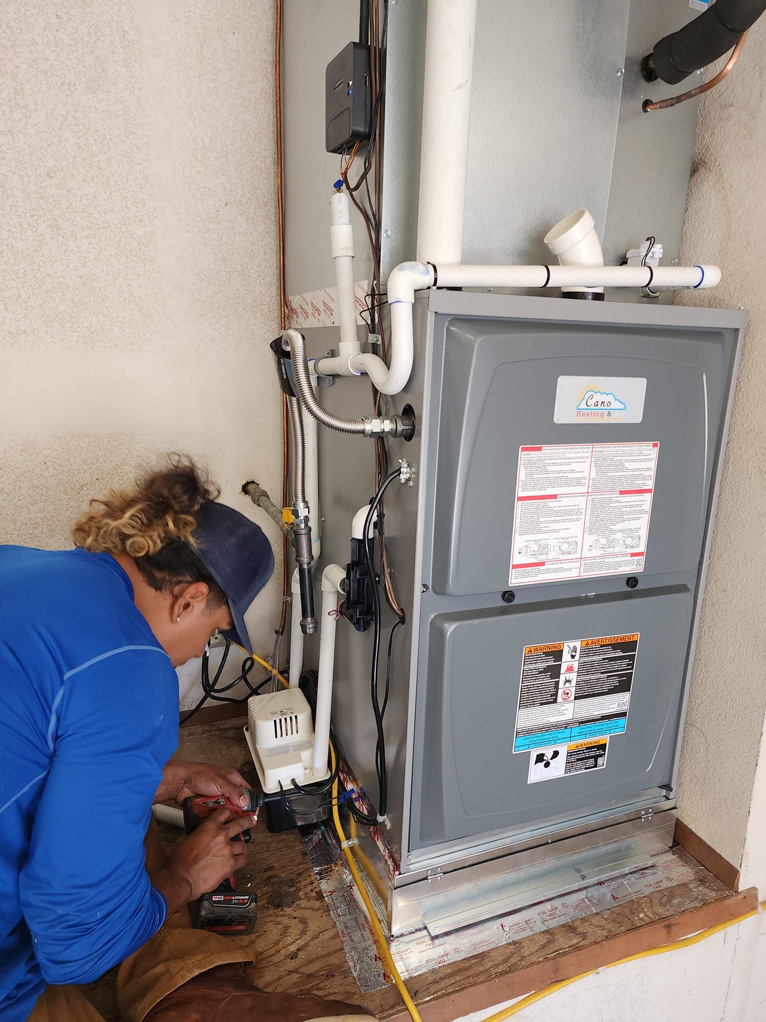 Person in blue shirt working on a furnace in a beige room.