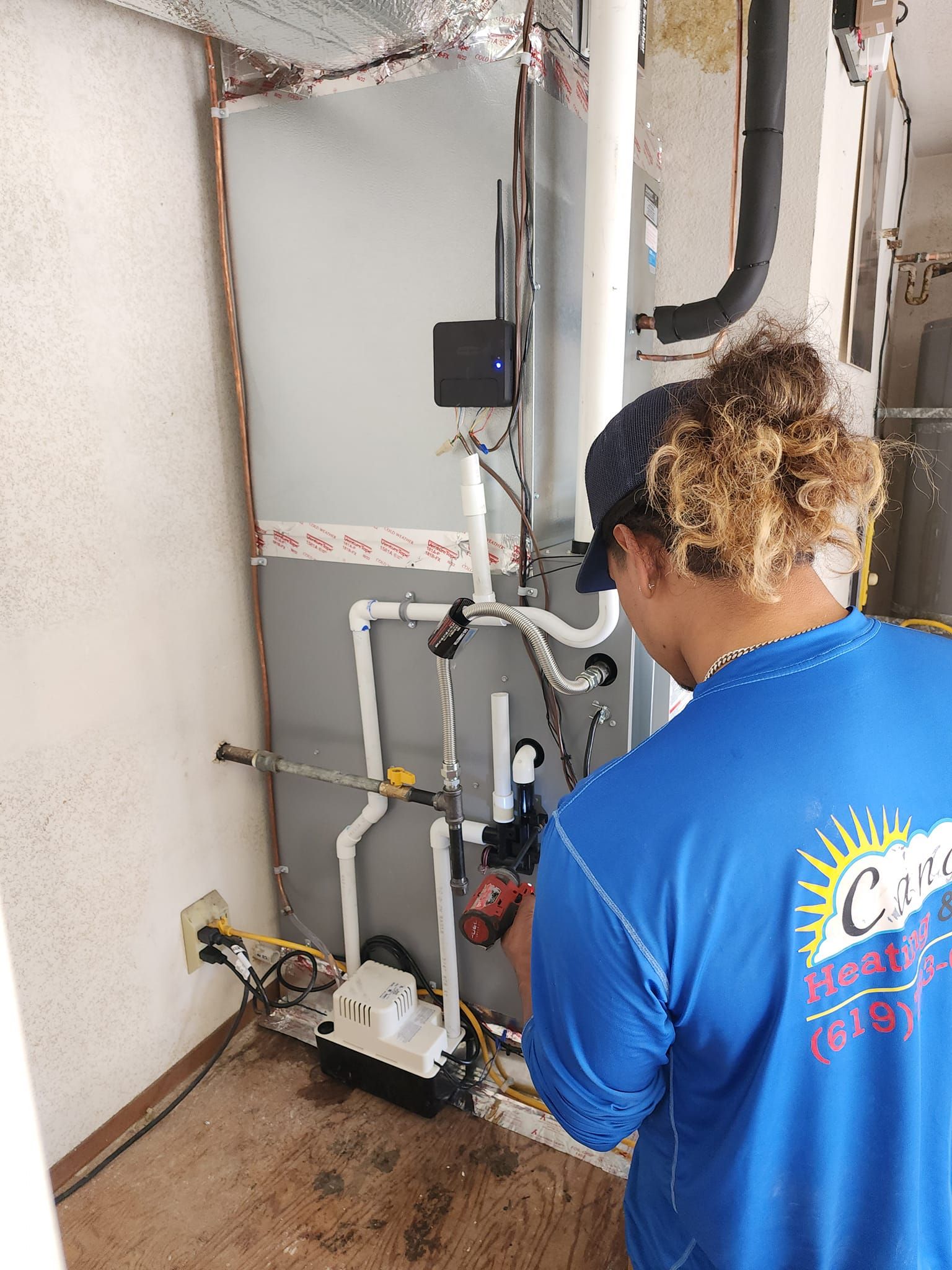 Person in blue shirt working on a heating system. Plumbing and electrical components are visible.