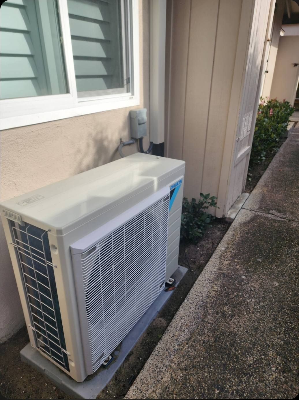 Outdoor air conditioning unit next to a building, by a window.