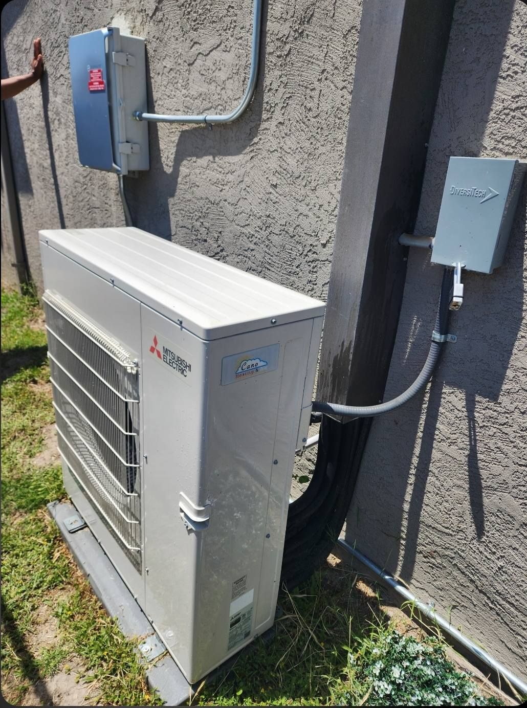 Mitsubishi heat pump unit outside a building with electrical boxes.