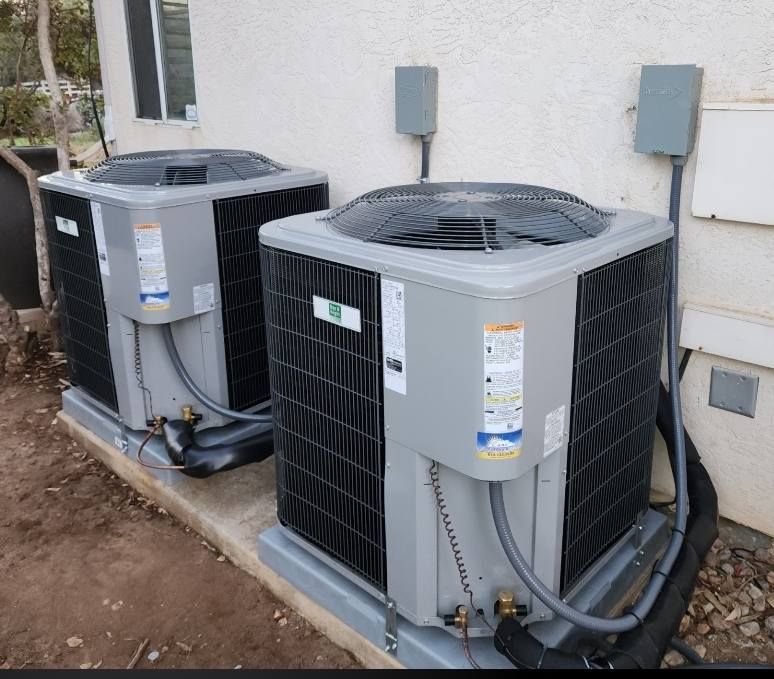 Two air conditioning units side-by-side on a concrete pad next to a light-colored wall.