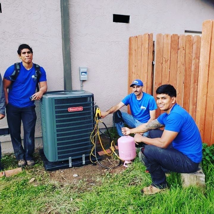 Three people in blue shirts working on an AC unit outdoors. One holds a pink tank.