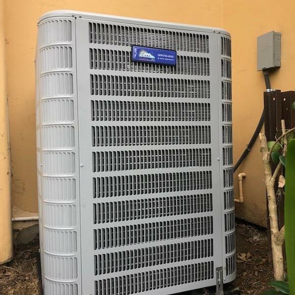 Outdoor air conditioning unit against a light brown wall.