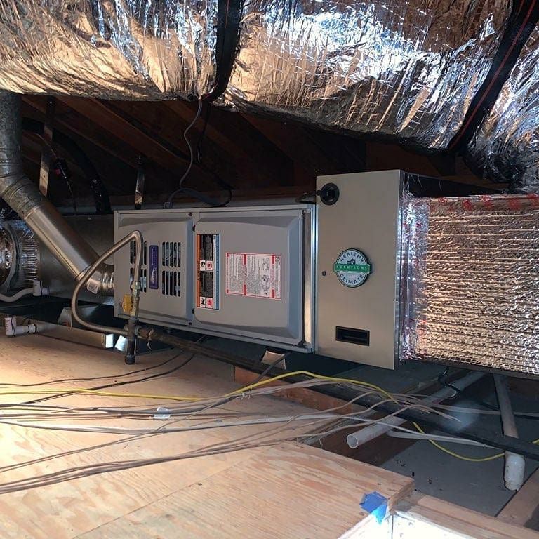 HVAC unit in an attic with ductwork, insulation, and wiring.