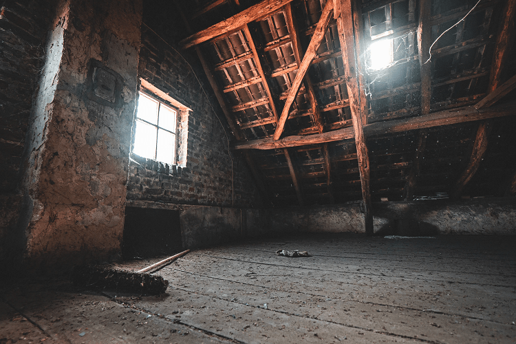 Dusty attic interior with wooden beams, a small window, and dim lighting.