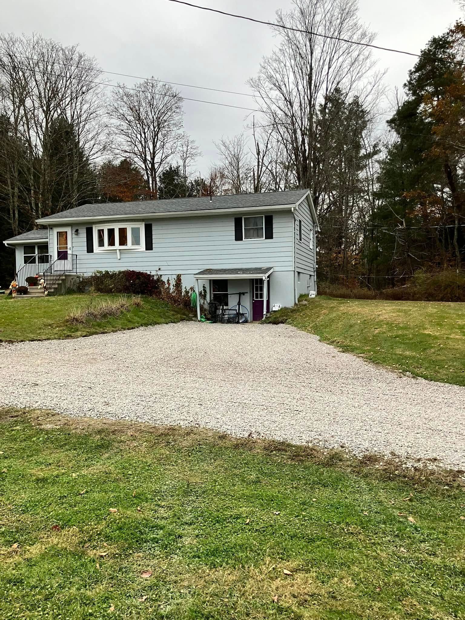 White split-level house with gravel driveway, grassy yard, and trees in fall