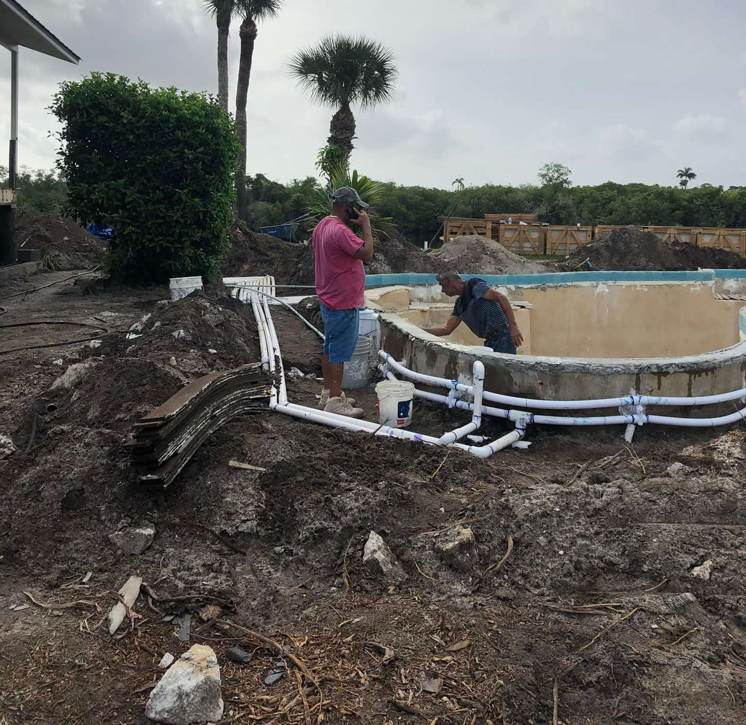 Workers installing white PVC pipes around a circular concrete tank at a muddy construction site.