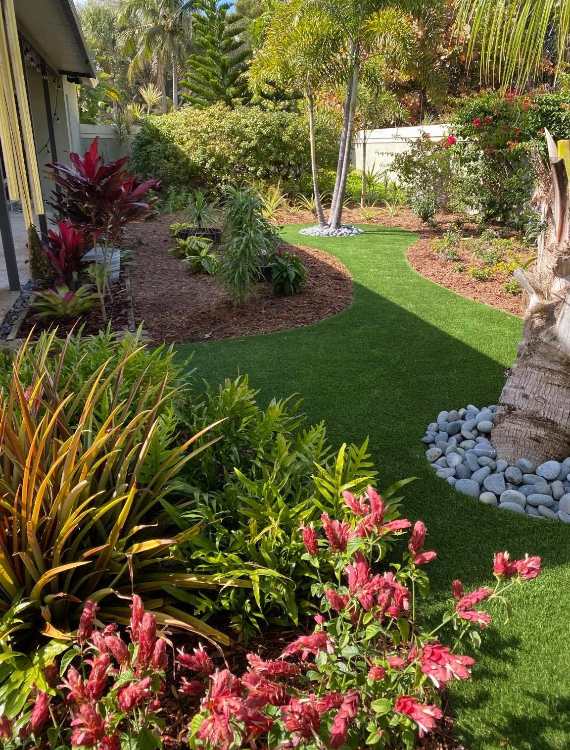 Lush tropical garden with green lawn, colorful flowers, and palm trees along a curved pathway