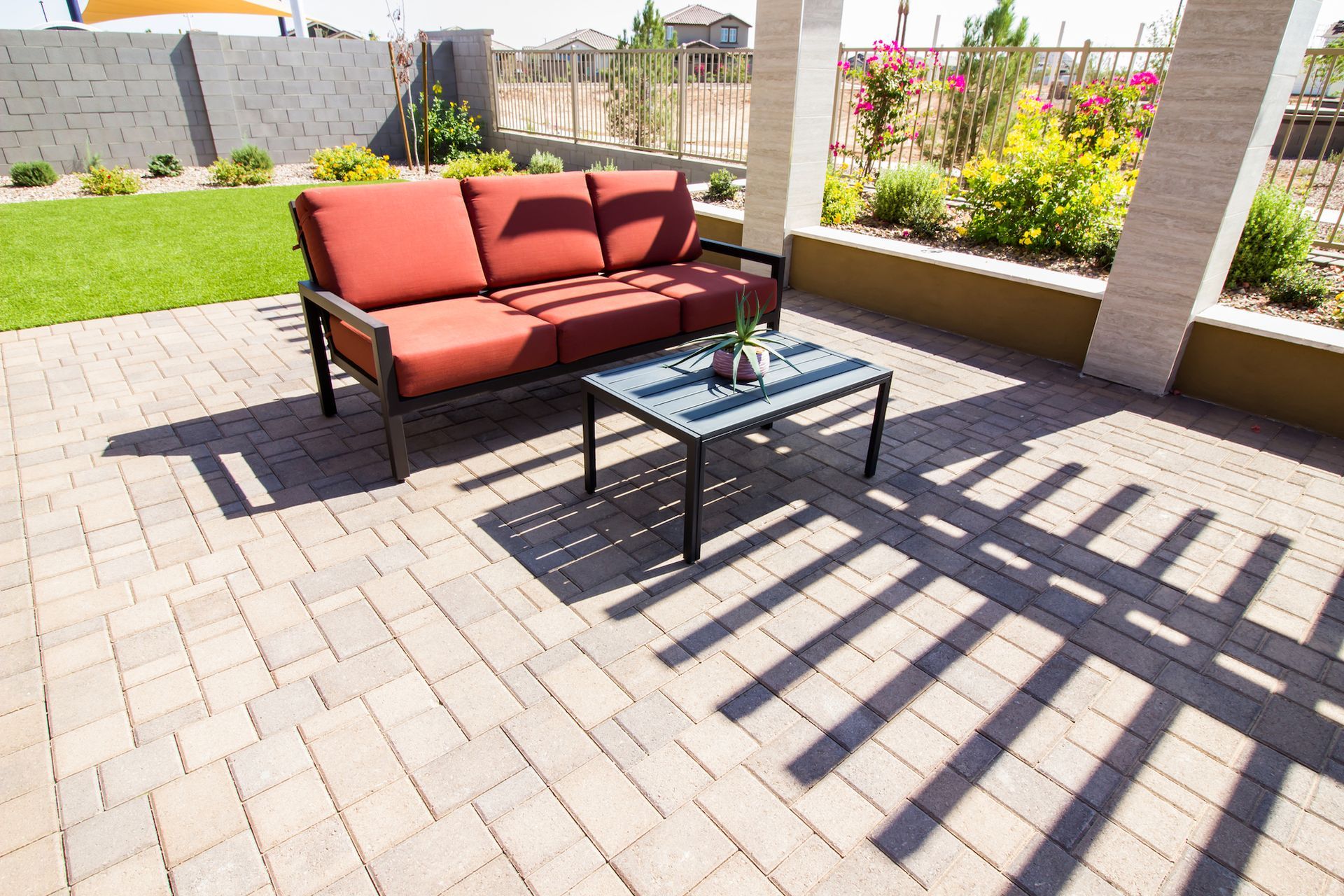 Patio with red outdoor sofa, glass coffee table, and striped shadows on brick pavers